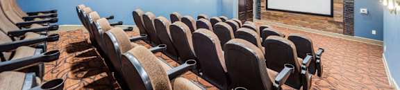 A row of black chairs are arranged in front of a screen in a dark room. at Reserve at Gulf Hills Apartment Homes in Ocean Springs, MS