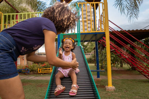 a mother playing with her daughter on a slide at a park at Cambridge Village in Houston, TX