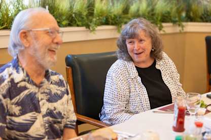 An older man and woman are sitting at a table and smiling.