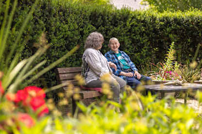 Two people sitting on a bench in a garden.