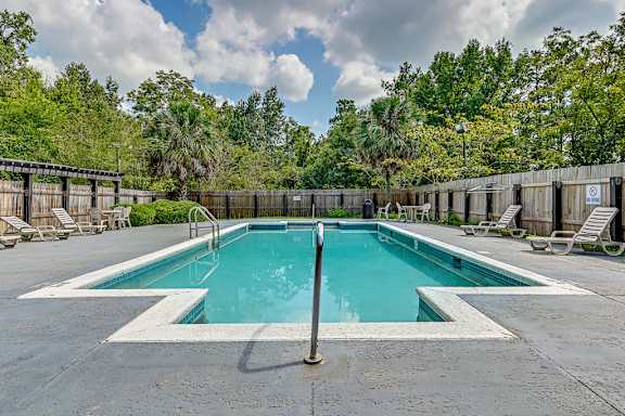 A large outdoor swimming pool surrounded by a wooden fence and lounge chairs.