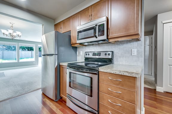 a kitchen with wood cabinets and stainless steel appliances at Village at The Pointe Apartments, Tacoma, WA,98407
