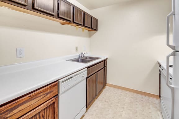 A kitchen with white appliances, light counter, and spacious wooden cabinets at Ladera Villa Apartments.
