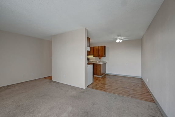 An empty white living room with a kitchen in the corner at Cedar Gardens Apartments. 