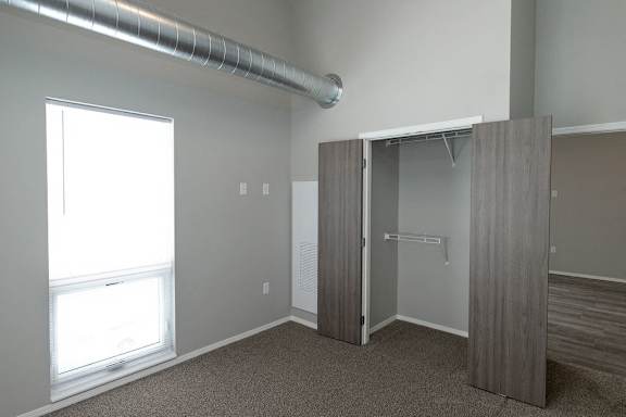 A room with a window, a carpeted floor, and a closet with a sliding door.