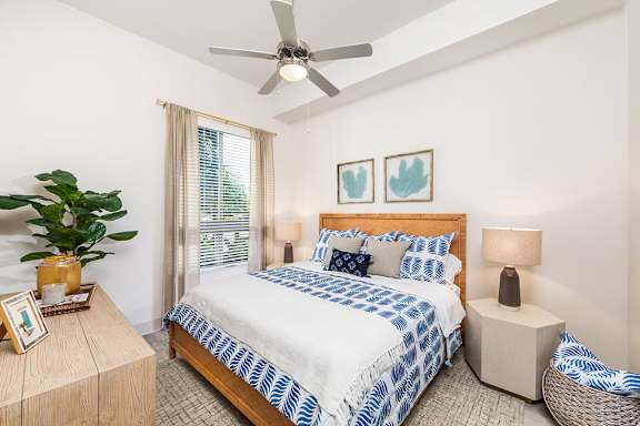 A bedroom with a bed, a ceiling fan, and a plant on a table. at Morea Apartments, Pompano Beach, Florida