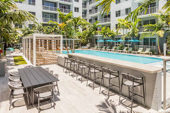 A poolside bar area with a wooden table and chairs. at Morea Apartments, Pompano Beach, Florida