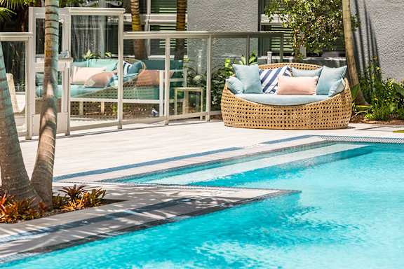 A pool with a wicker chair and a cushion on it. at Morea Apartments, Pompano Beach, Florida