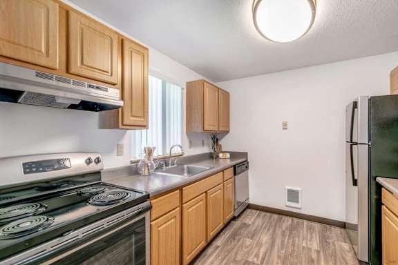 A kitchen with wooden cabinets and a black stove top oven.at Alder Creek Apartments, Washington