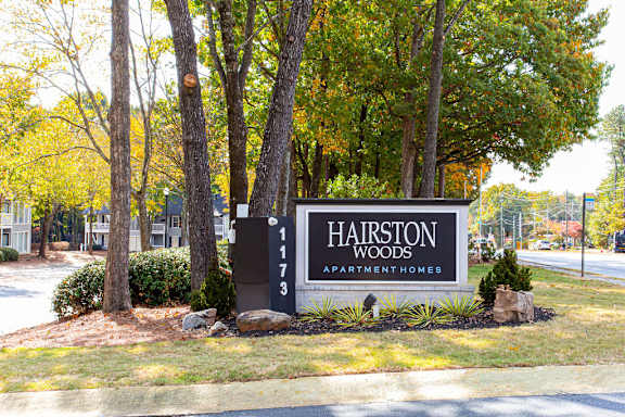 A sign for Hairston Woods Apartment Homes is in front of a row of trees.