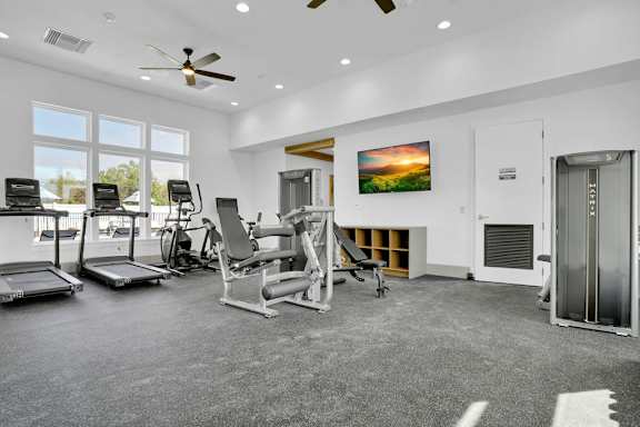 A spacious gym with a variety of equipment and a large window overlooking the outdoors.