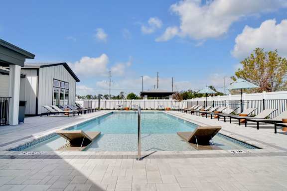 A large outdoor swimming pool with sun loungers and a building in the background.
