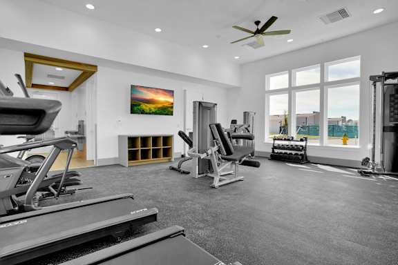 A spacious gym with treadmills, weights, and a ceiling fan.