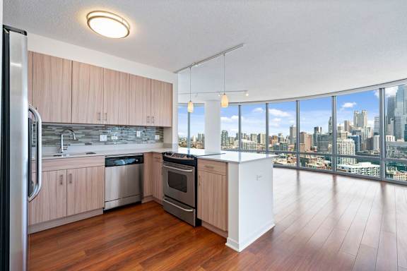 A modern kitchen with wooden floors and a large window overlooking the city.