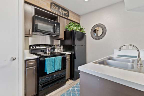Compact kitchen with black appliances and wood style flooring at The Colony Apartments, Universal City, Texas