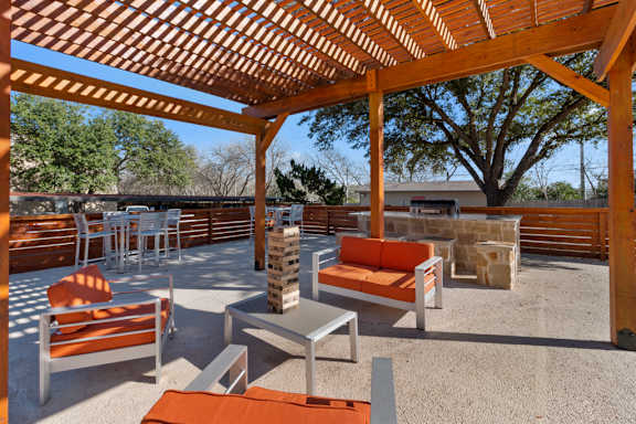 Outdoor lounge with pergola and stone fireplace at The Colony Apartments, Universal City, 78148
