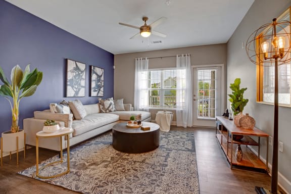 Living room with hard wood floors, couch, rug, tables and big windows.