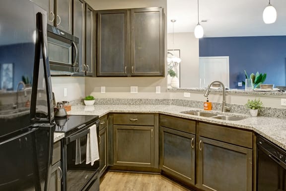 Kitchen with dark cabinets, black appliances, sink , granite countertops, and light hard wood flooring at Ascent at Mallard Creek Charlotte, NC