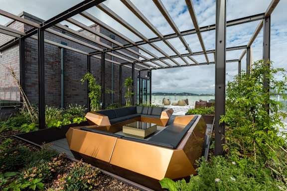 A modern outdoor seating area with a glass roof and metal frame at Beton Apartments, Wembley, HA9 0SL