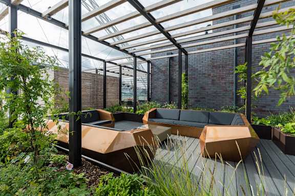A modern outdoor seating area with wooden benches and a glass roof at Beton Apartments, Wembley, HA9 0SL