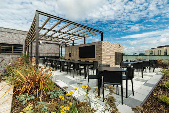 A modern outdoor seating area with black chairs and tables at Beton Apartments, Wembley, HA9 0SL