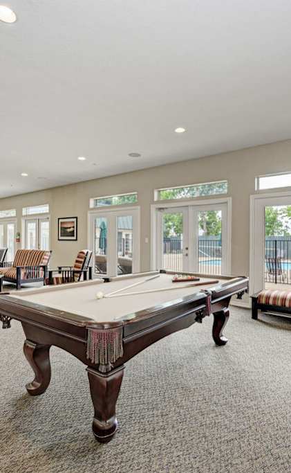 A billiard table is in the middle of a room with striped couches and a television.