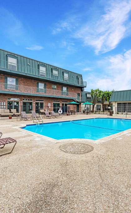 A pool surrounded by lounge chairs and umbrellas in front of a building.