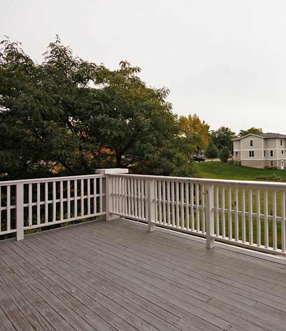 A wooden deck with a white railing overlooks a green lawn and a house.