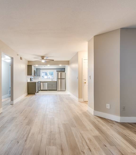 the living room and kitchen of an empty apartment with wood floors and a ceiling fan