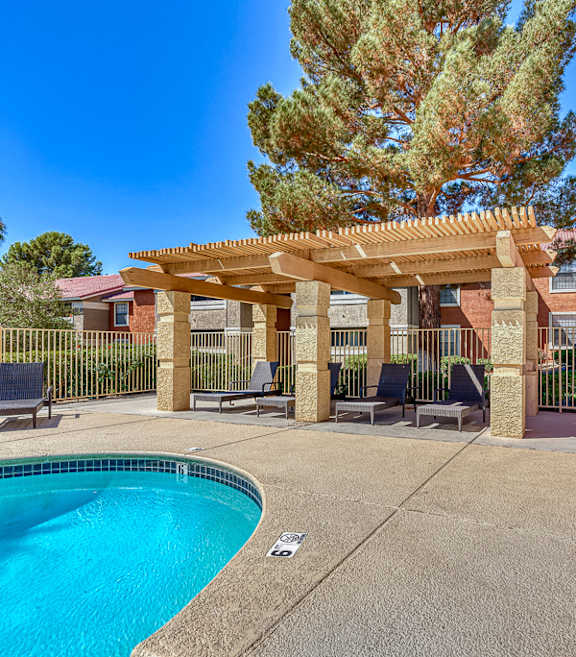 A pool area with a wooden pergola and a tree in the background.