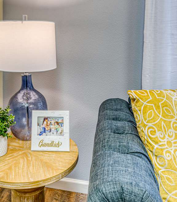 A blue lamp with a white lampshade sits on a wooden table next to a small potted plant and a picture frame with the word "Chandler's" on it.
