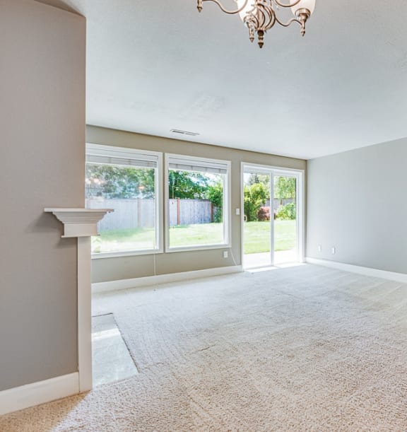 an empty living room with large windows and a chandelier