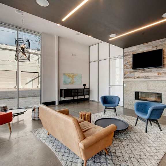 The amazing resident lounge with a fireplace, orange couches, decorations, large windows, red and blue plush chairs, and coffee tables at Stitchweld Apartment Homes. 