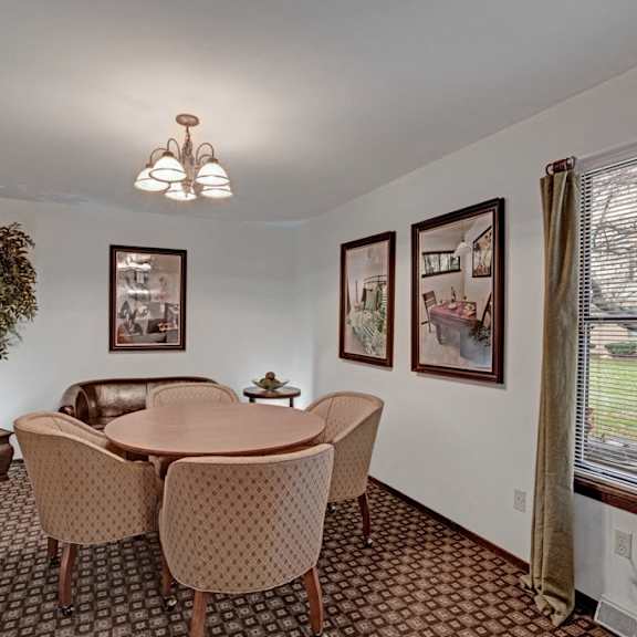 The seating area with a circular table surrounded by plush chairs and a love seat behind them at Sunset Ridge Apartments. 
