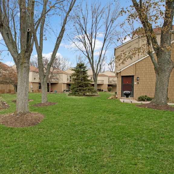 Green space with trees surrounding the tan apartment buildings at Sunset Ridge Apartments. 