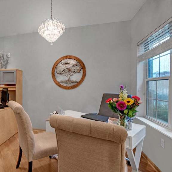 A front office with a light wood a desktop computer and decorations and common area with a smaller desk and chairs with a flower vase at Swan Creek Apartment Homes. 