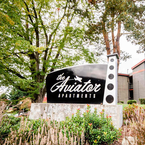 The sign for The Aviator Apartments is in front of a building.
