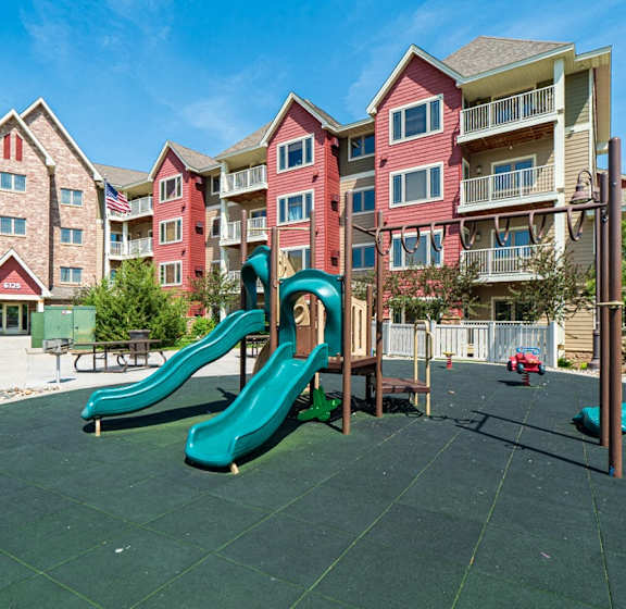 A playground with a green slide in front of apartment buildings.