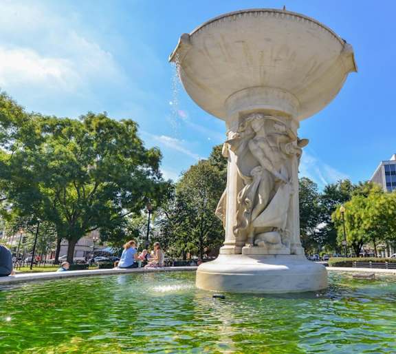 A large fountain in the middle of a park with people sitting around it.