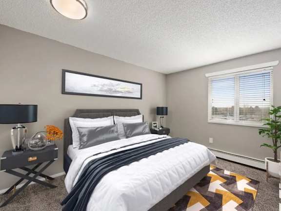 A bedroom with a large bed, a nightstand with a lamp, and a framed picture on the wall.