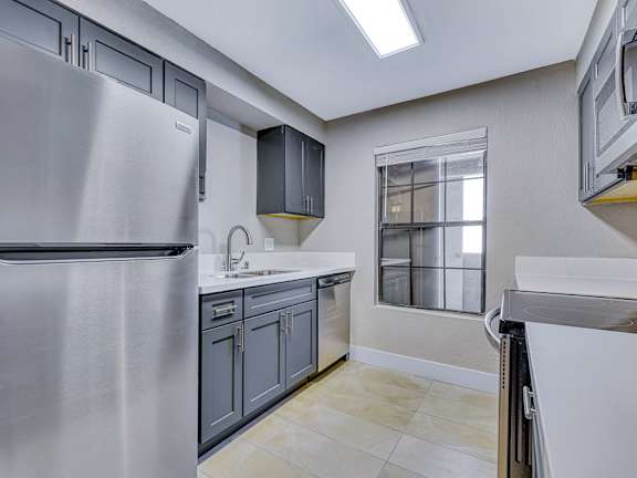 A modern kitchen with a stainless steel refrigerator and grey cabinets.
