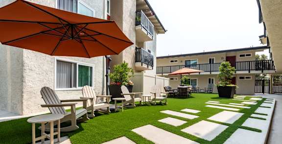 a patio with chairs and an umbrella in front of an apartment building at Parkway Terrace Apartments, Culver City, 90230