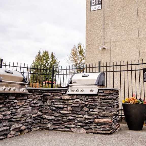 A stone wall with two BBQ grills on top and a black fence.