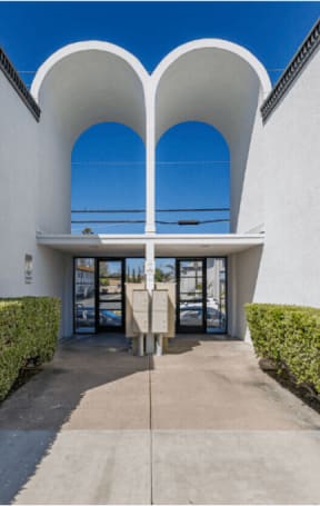 a walkway leading to the entrance of a white building with blue skiesat The Arches Apartments, LLC, El Cajon, CA