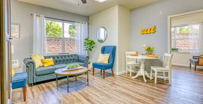 A living room with a green couch, a blue chair, a white dining table and chairs, and a ceiling fan.
