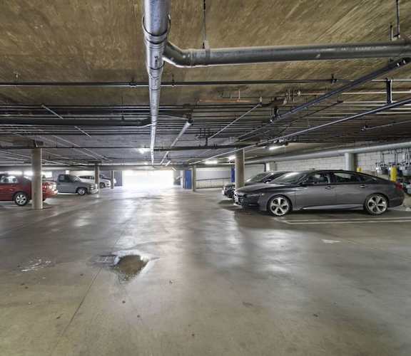 A parking garage with a few cars and a puddle on the floor.