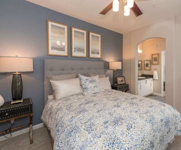 A fully furnished blue and white bedroom with a bed and a ceiling fan and nightstands. 