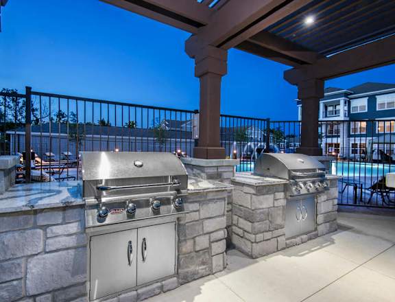 A stone patio with two built-in BBQ grills under a roof. at Steele Crossing, Fayetteville, Arkansas