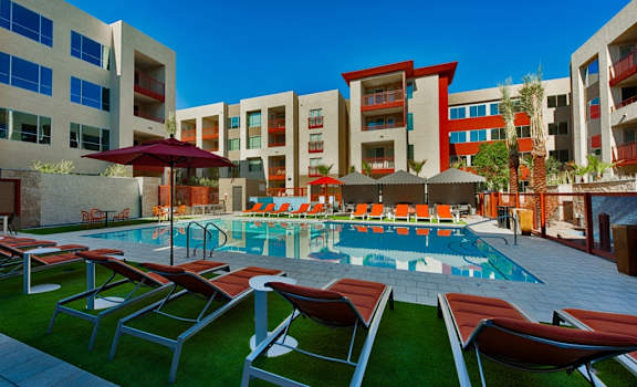 a swimming pool with lounge chairs and umbrellas in front of an apartment building at Elevation on Central Apartments, Phoenix, AZ, 85012
