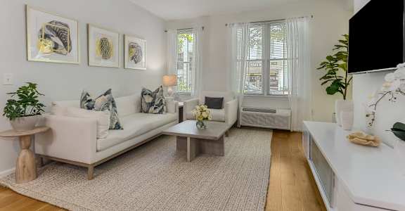 A living room with a white couch, a coffee table, and a flat screen TV mounted on the wall.
